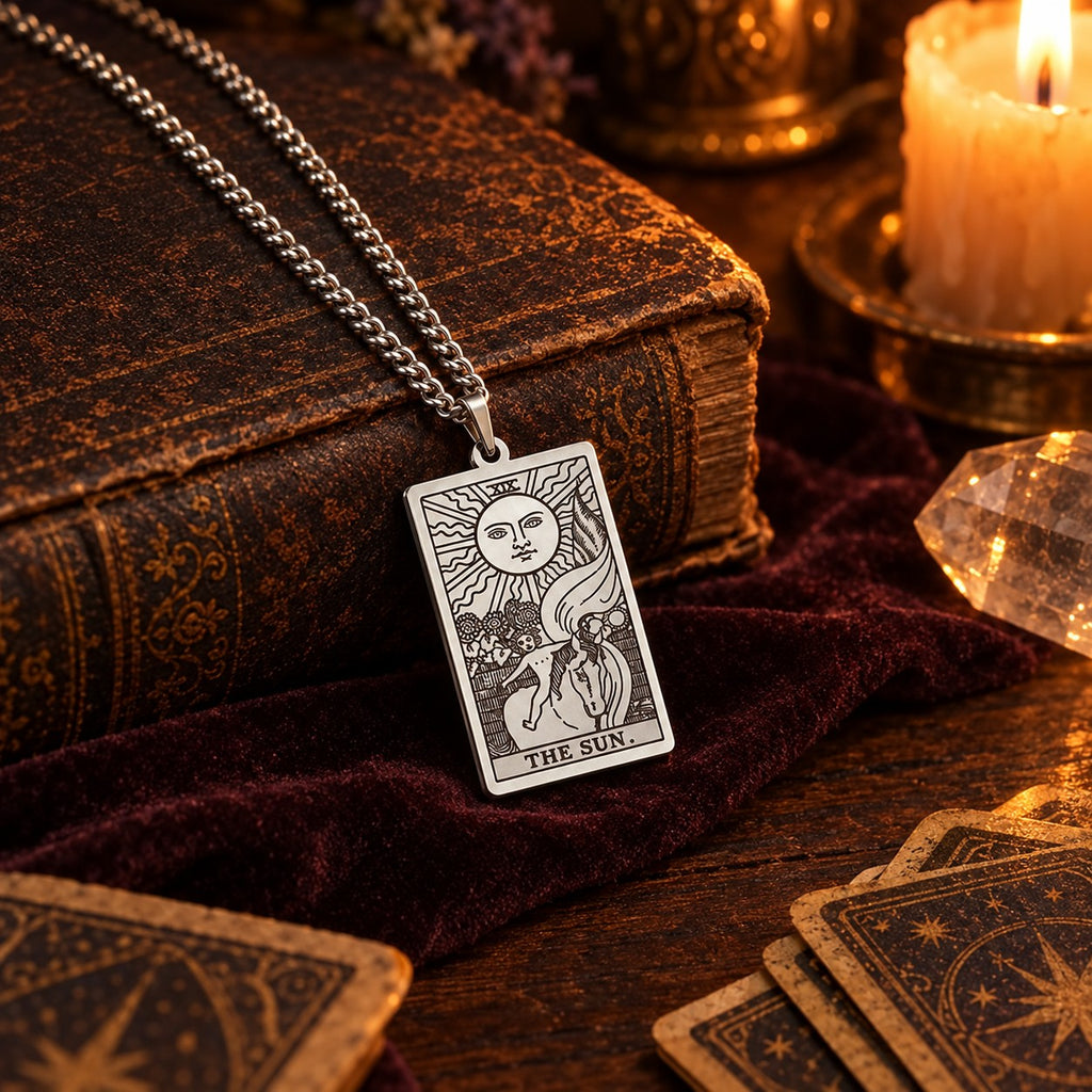 Silver The Sun tarot card pendant necklace resting on an antique leather book beside a candle and tarot cards